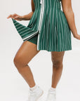 A woman wearing a sleeveless, pinstripe green dress with a pleated skirt, white trim, and applique logos.