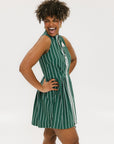 A woman wearing a sleeveless, pinstripe green dress with a pleated skirt, white trim, and applique logos.