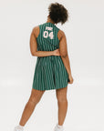 A woman wearing a sleeveless, pinstripe green dress with a pleated skirt, white trim, and applique logos.
