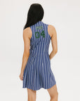 A person standing against a white background wearing a blue sleeveless dress with white pinstripes and a round neckline.