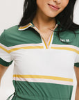 A woman in a green, white, and yellow striped polo dress with a ribbed collar and elastic toggles at the waist. The dress features side seam pockets and a branding stripe.