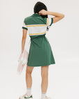 A woman in a green, white, and yellow striped polo dress with a ribbed collar and elastic toggles at the waist. The dress features side seam pockets and a branding stripe.