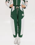 A pair of color-blocked green and white warm-up pants with a pink stripe, featuring a flat drawstring waistband and deep front pockets, branded with the 'Fore All' detail on the back and an FA icon on the inner calf.