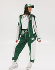 A pair of color-blocked green and white warm-up pants with a pink stripe, featuring a flat drawstring waistband and deep front pockets, branded with the 'Fore All' detail on the back and an FA icon on the inner calf.