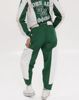 A pair of color-blocked green and white warm-up pants with a pink stripe, featuring a flat drawstring waistband and deep front pockets, branded with the 'Fore All' detail on the back and an FA icon on the inner calf.