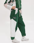 A pair of color-blocked green and white warm-up pants with a pink stripe, featuring a flat drawstring waistband and deep front pockets, branded with the 'Fore All' detail on the back and an FA icon on the inner calf.