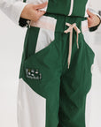 A pair of color-blocked green and white warm-up pants with a pink stripe, featuring a flat drawstring waistband and deep front pockets, branded with the 'Fore All' detail on the back and an FA icon on the inner calf.