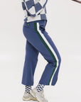 A person wearing the Simone Pant in blue with white stripes on the side, featuring princess seams down the leg and a slit at the hem. The person is also wearing a checkered blue and white top and white sneakers.