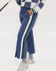 A person wearing the Simone Pant in blue with white stripes on the side, featuring princess seams down the leg and a slit at the hem. The person is also wearing a checkered blue and white top and white sneakers.