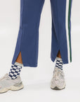 A person wearing the Simone Pant in blue with white stripes on the side, featuring princess seams down the leg and a slit at the hem. The person is also wearing a checkered blue and white top and white sneakers.