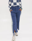 A person wearing the Simone Pant in blue with white stripes on the side, featuring princess seams down the leg and a slit at the hem. The person is also wearing a checkered blue and white top and white sneakers.