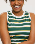 A woman smiling and wearing a sleeveless tank top with green and yellow stripes and a solid white neckline and armholes.