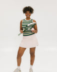 A woman smiling and wearing a sleeveless tank top with green and yellow stripes and a solid white neckline and armholes.