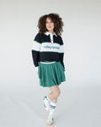 A person wearing a long sleeve polo shirt with horizontal green and white stripes and the text 'Golfing Optional' on the chest, paired with a green skirt.