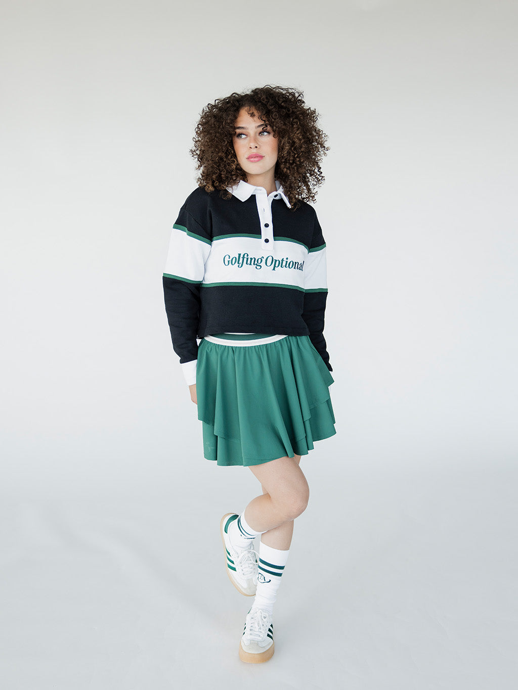 A person wearing a long sleeve polo shirt with horizontal green and white stripes and the text 'Golfing Optional' on the chest, paired with a green skirt.