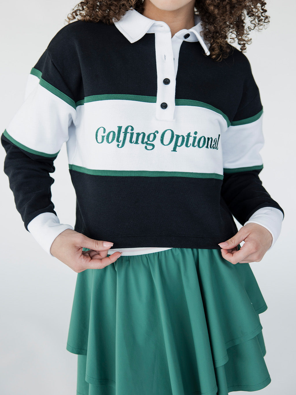 A person wearing a long sleeve polo shirt with horizontal green and white stripes and the text 'Golfing Optional' on the chest, paired with a green skirt.