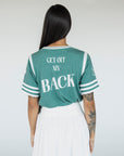 A woman wearing a green sporty top with text 'Fore All 04' and stripes, paired with a white skirt.