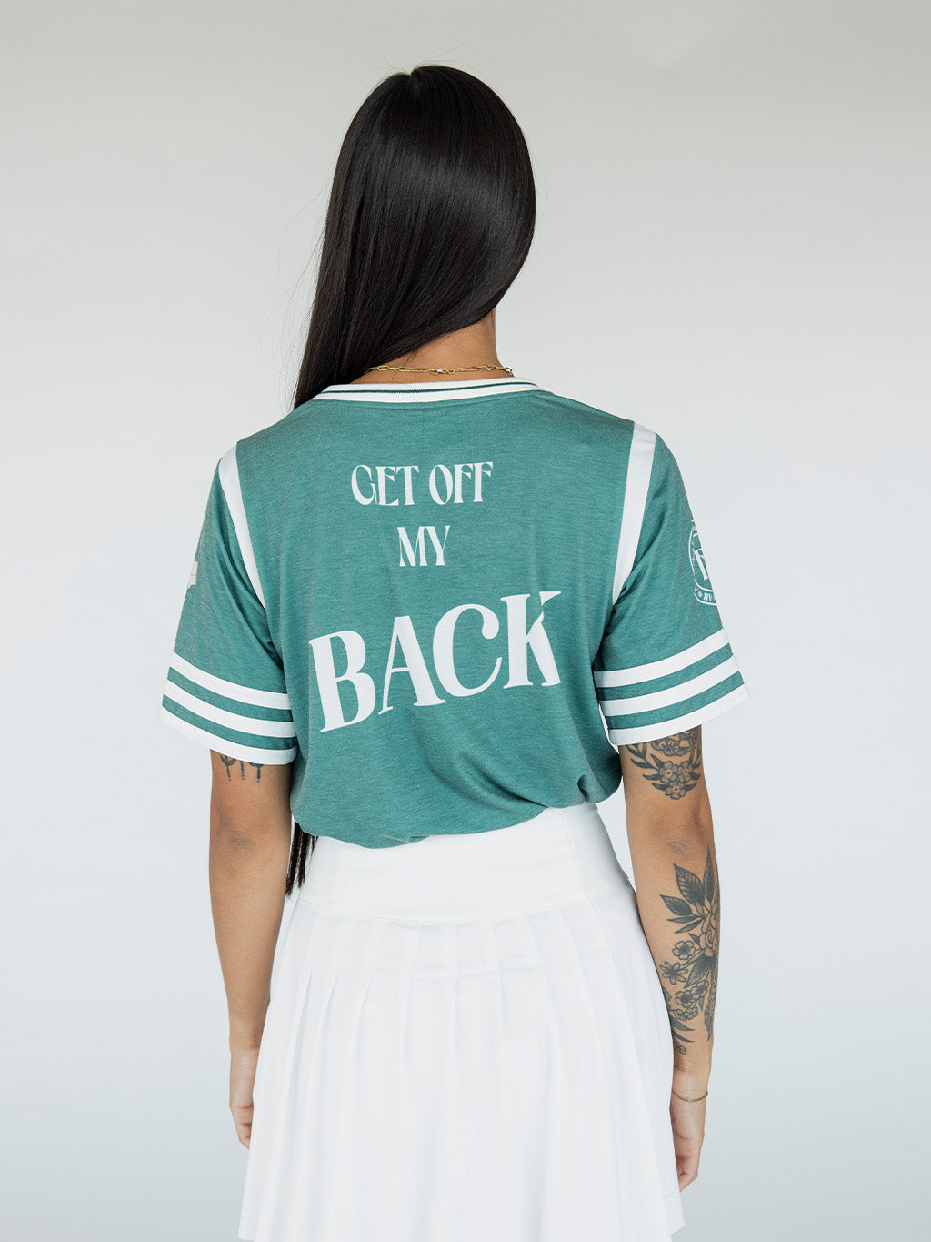 A woman wearing a green sporty top with text 'Fore All 04' and stripes, paired with a white skirt.