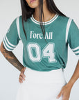 A woman wearing a green sporty top with text 'Fore All 04' and stripes, paired with a white skirt.