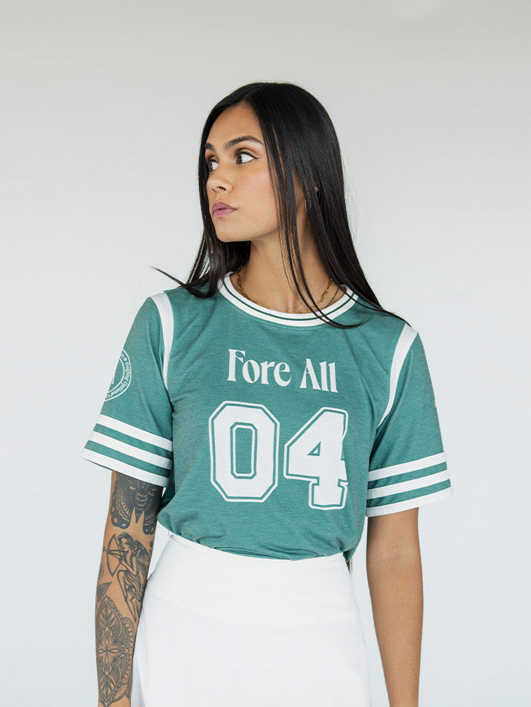 A woman wearing a green sporty top with text 'Fore All 04' and stripes, paired with a white skirt.