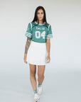 A woman wearing a green sporty top with text 'Fore All 04' and stripes, paired with a white skirt.