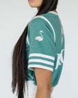 A woman wearing a green sporty top with text 'Fore All 04' and stripes, paired with a white skirt.