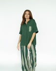 A woman wearing a green button-up shirt with a collar and front pocket, paired with striped pants.