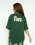 A person wearing a green button-up shirt with the word 'Fore' embroidered on the back.