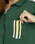 A woman wearing a green button-up shirt with a collar and front pocket, paired with striped pants.