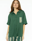 A woman wearing a green button-up shirt with a collar and front pocket, paired with striped pants.