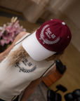 A person wearing a burgundy and white baseball cap with text and leaf patterns.