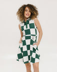 A woman wearing a green and white checkered sleeveless dress with a button placket and side seam pockets.