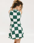 A woman wearing a green and white checkered sleeveless dress with a button placket and side seam pockets.