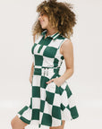 A woman wearing a green and white checkered sleeveless dress with a button placket and side seam pockets.