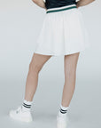 A woman wearing a white pleated golf skirt with a dark color waistband, paired with a gray top and white sneakers.