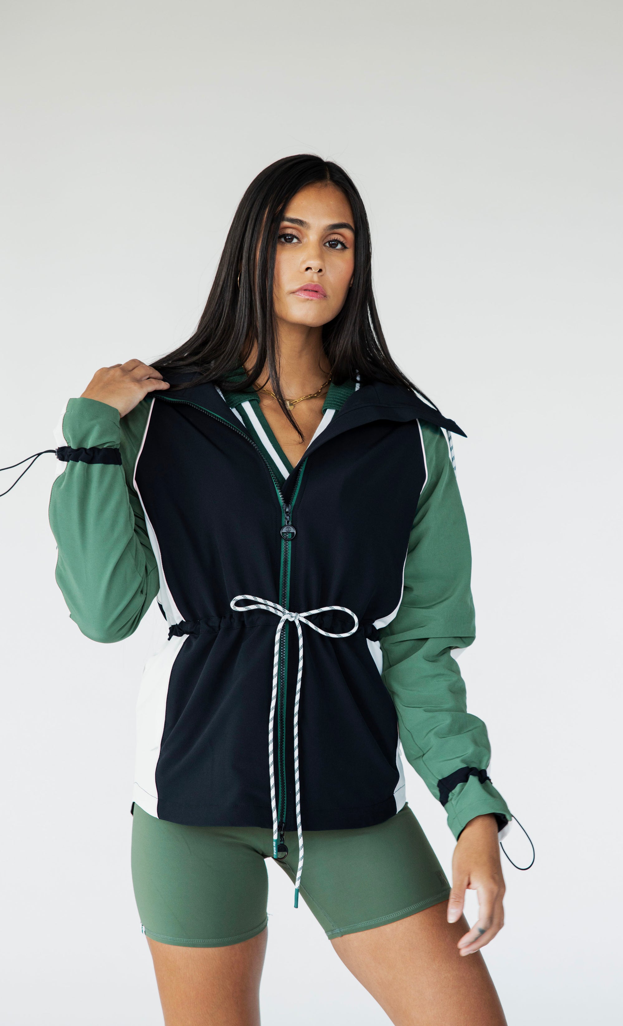 A female model wearing a black rain jacket with green sleeves, featuring a high neck, water-resistant properties, and a double zipper closure.