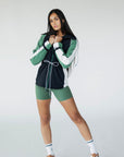 A female model wearing a black rain jacket with green sleeves, featuring a high neck, water-resistant properties, and a double zipper closure.