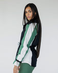 A female model wearing a black rain jacket with green sleeves, featuring a high neck, water-resistant properties, and a double zipper closure.