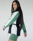 A female model wearing a black rain jacket with green sleeves, featuring a high neck, water-resistant properties, and a double zipper closure.