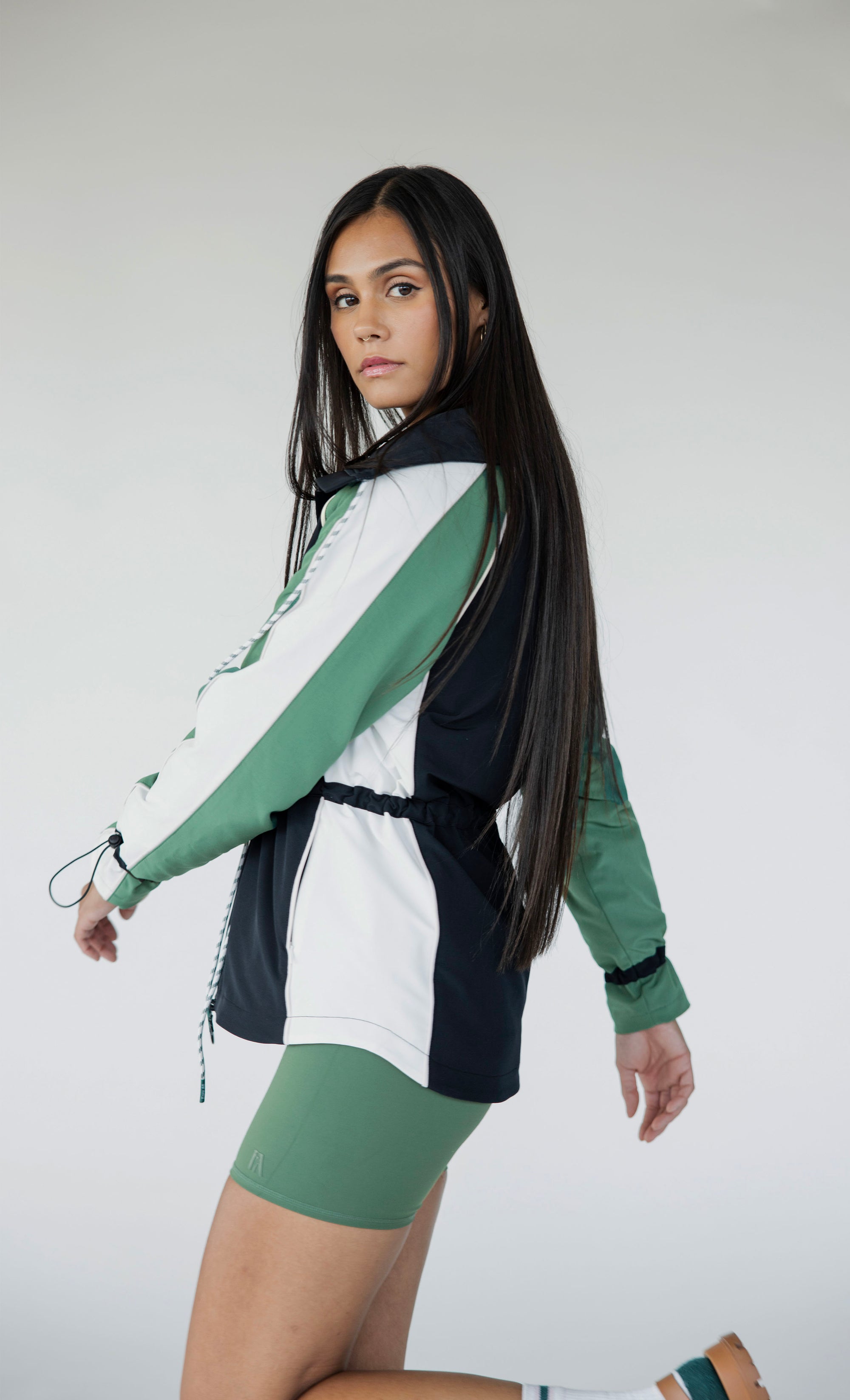A female model wearing a black rain jacket with green sleeves, featuring a high neck, water-resistant properties, and a double zipper closure.