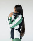 A female model wearing a black rain jacket with green sleeves, featuring a high neck, water-resistant properties, and a double zipper closure.