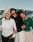 Three women wearing dorothy sweaters on a dock.