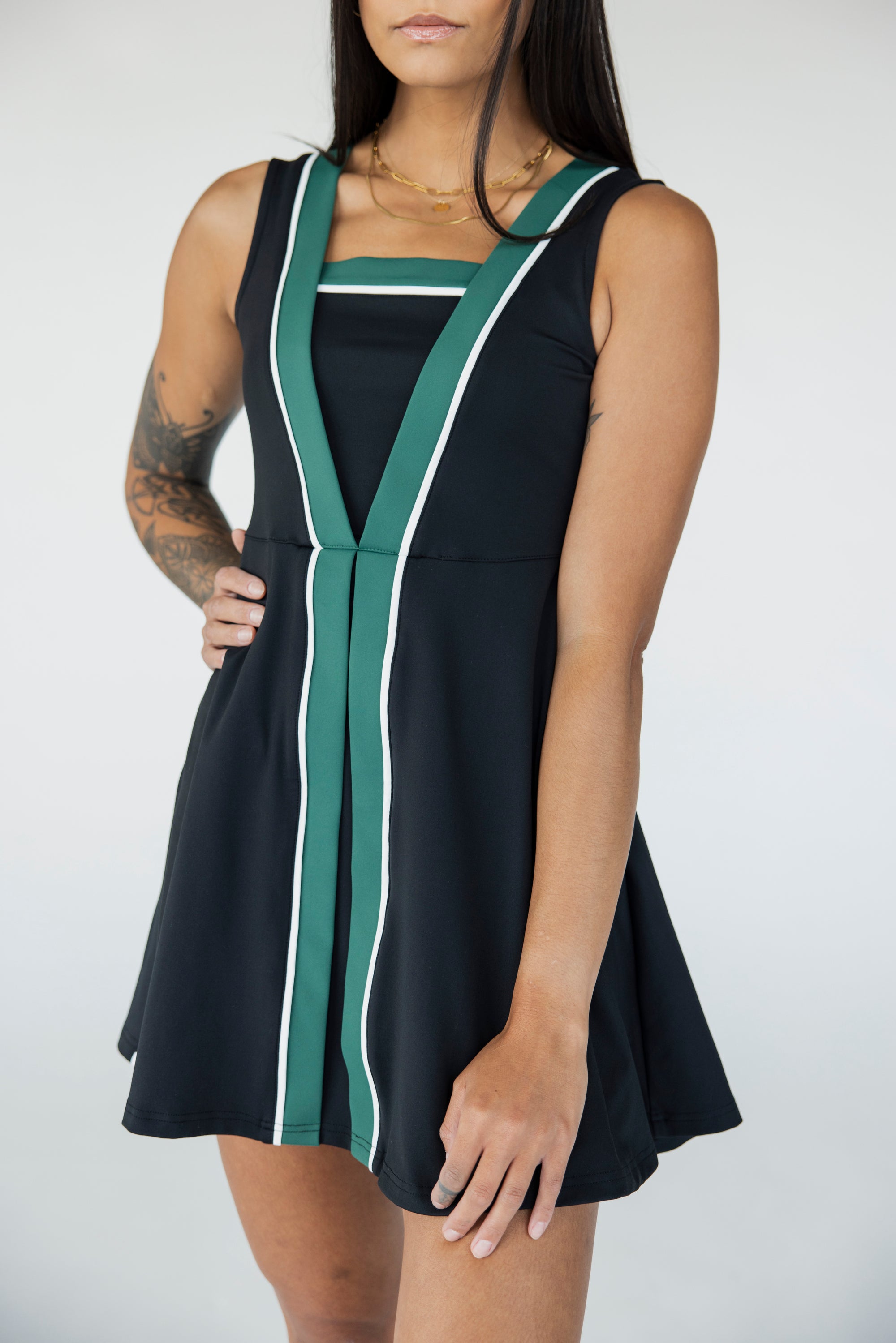 A model wearing a black sleeveless dress with a green vertical stripe detail on the front, designed with a flattering silhouette.