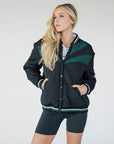 A female model wearing a black bomber jacket with color-blocked sunset design on the back, standing against a neutral background.