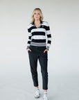 A woman wearing a black and white striped sweater with a V-neck collar and a small embroidered patch on the left chest.