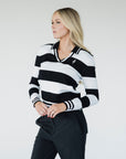 A woman wearing a black and white striped sweater with a V-neck collar and a small embroidered patch on the left chest.