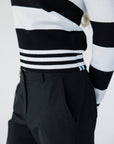 A woman wearing a black and white striped sweater with a V-neck collar and a small embroidered patch on the left chest.