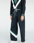 A model wearing a black sweatpant with green and white stripe details, paired with a matching sweatshirt.