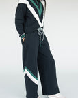 A model wearing a black sweatpant with green and white stripe details, paired with a matching sweatshirt.