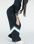 A model wearing a black sweatpant with green and white stripe details, paired with a matching sweatshirt.